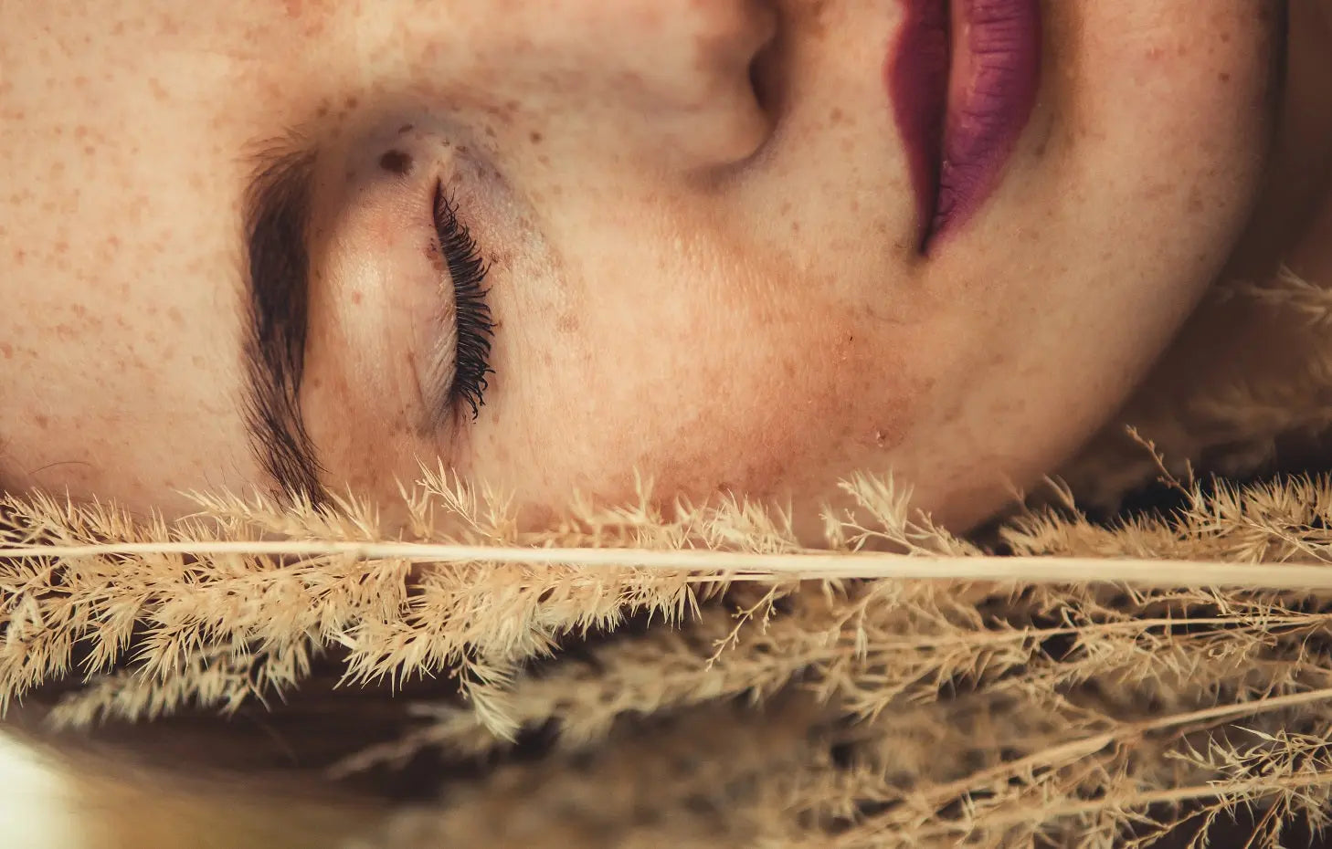Eine Frau mit geschlossenen Augen die neben ihrem Gesicht Gräser hat