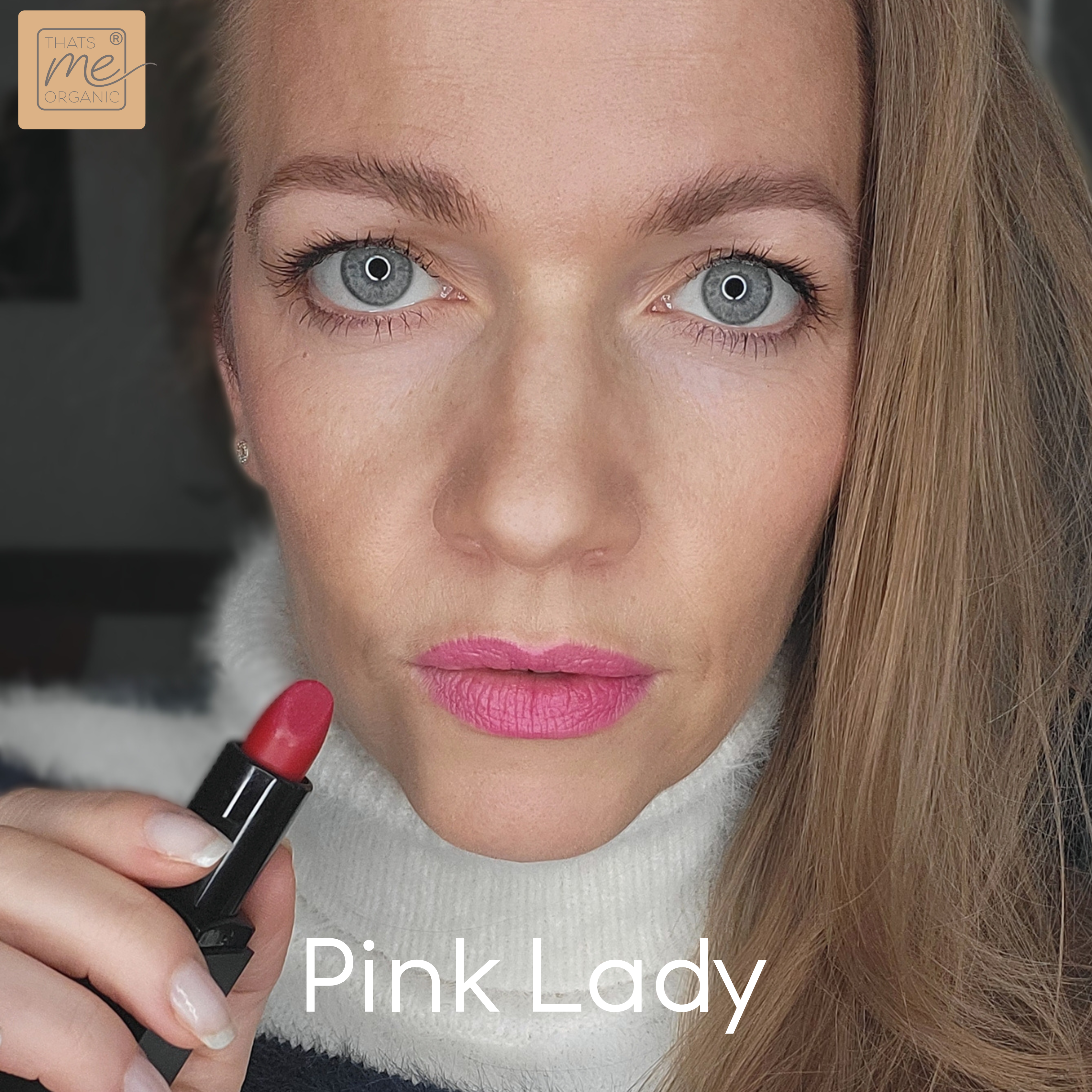 Eine Frau mit hellem Haar trägt rosa Lippenstift auf und trägt einen gestreiften Pullover. Der Text lautet: Pink Lady von Thats me Organic® - mit veganen Bio-Lippenstiften für natürliche Lippenpflege.