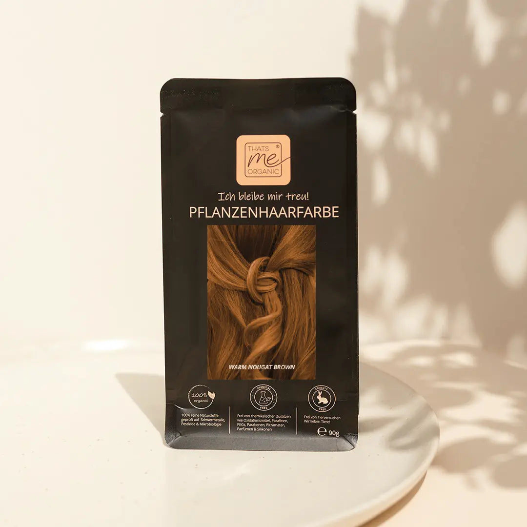 Eine schwarze Packung Haarfärbemittel auf Pflanzenbasis mit braunen Haarbildern, die auf einer weißen Fläche stehen.