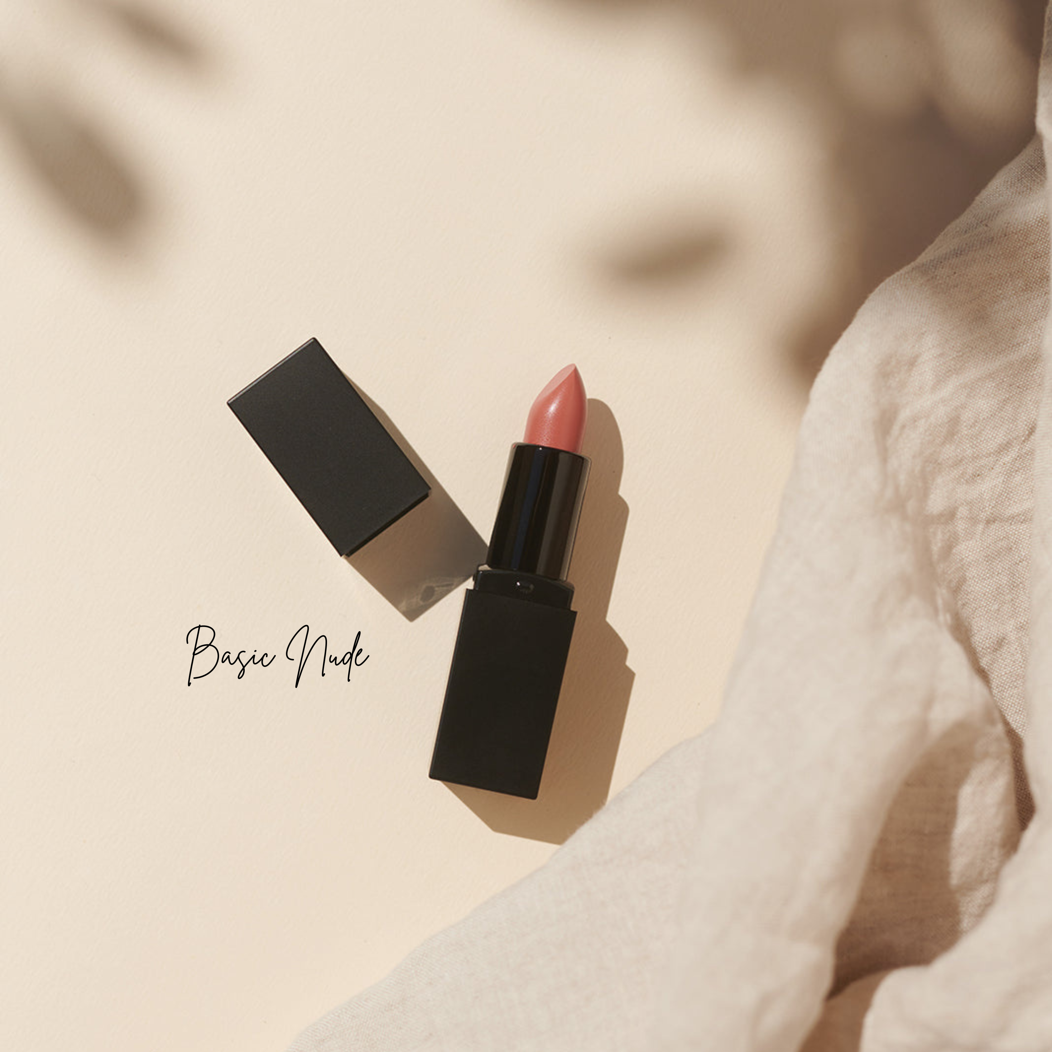 Ein nude-rosa Lippenstift von Thats me Organic® in einem schwarzen Etui liegt auf einer beigen Fläche neben hellem Stoff; der Text lautet Basic Nude - für natürliche Lippenpflege und vegane Bio-Lippenstifte.