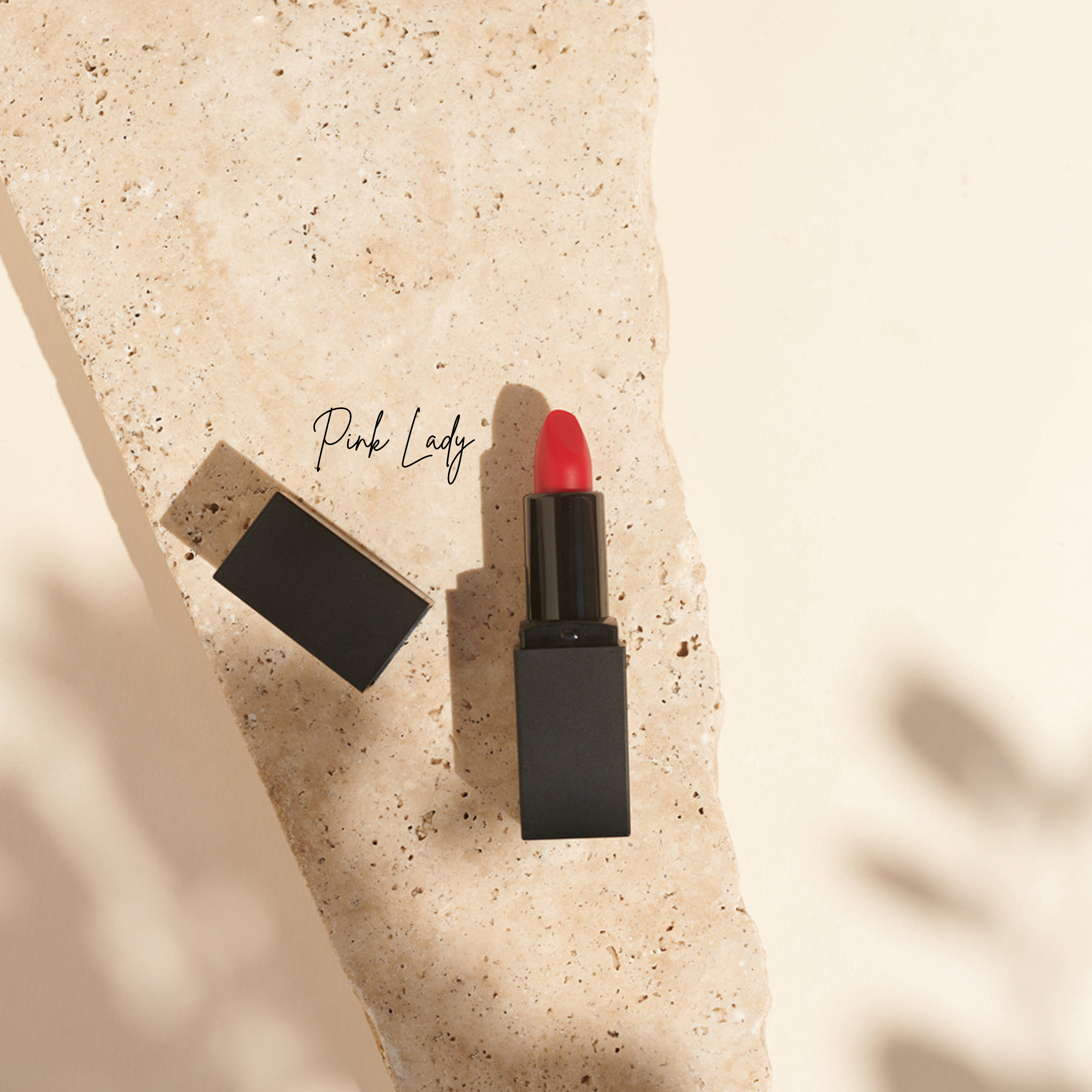 Ein roter, veganer Thats me Organic® Bio-Lippenstift mit einer schwarzen Kappe mit der Aufschrift Pink Lady ruht auf einer beigen Steinfläche.