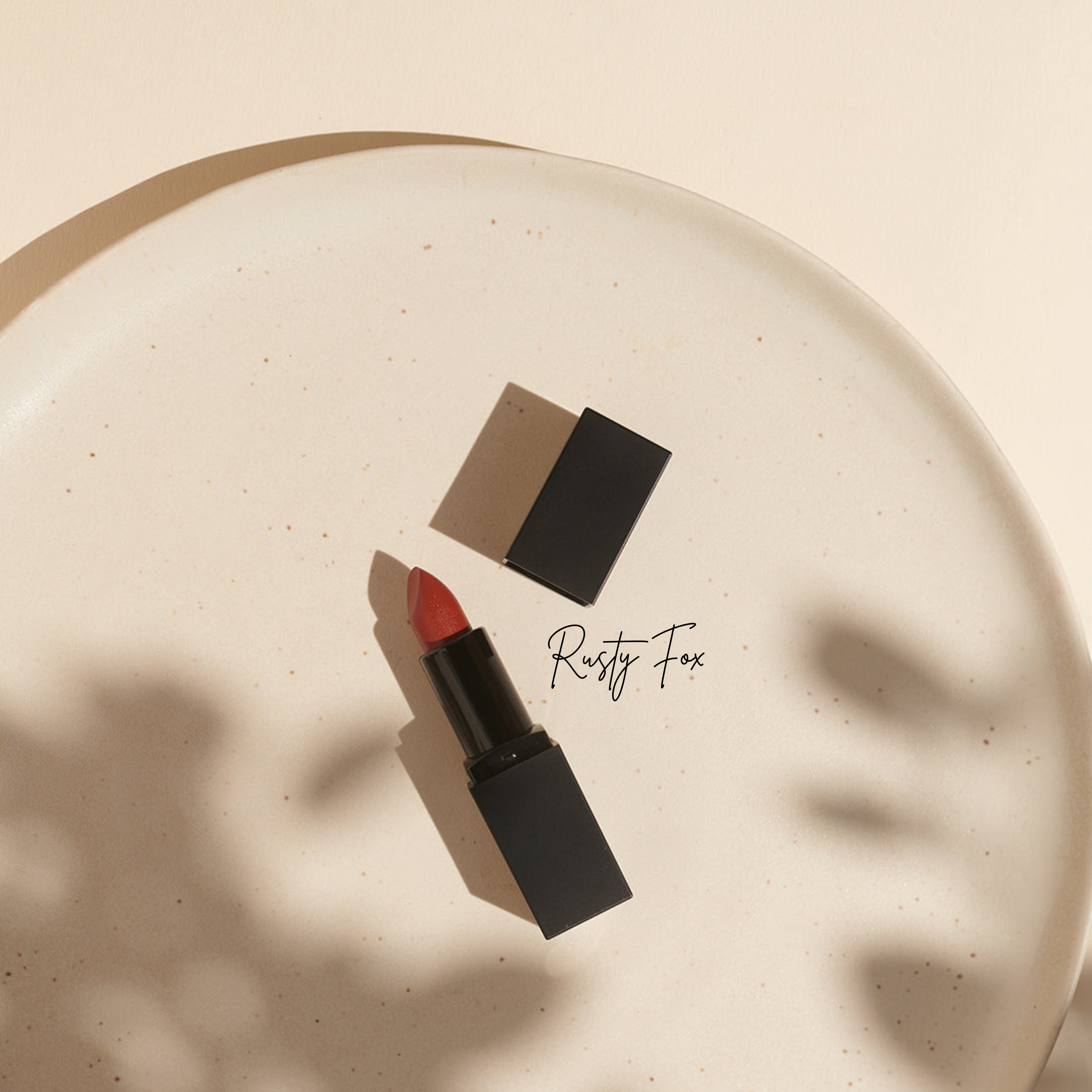 Mattschwarze Thats me Organic® Lippenstifthülse mit rotem Lippenstift auf einer gesprenkelten beigen Platte, daneben eine Kappe und weiche Schatten - ideal für Fans von veganen Bio-Lippenstiften, die natürliche Lippenpflege suchen.