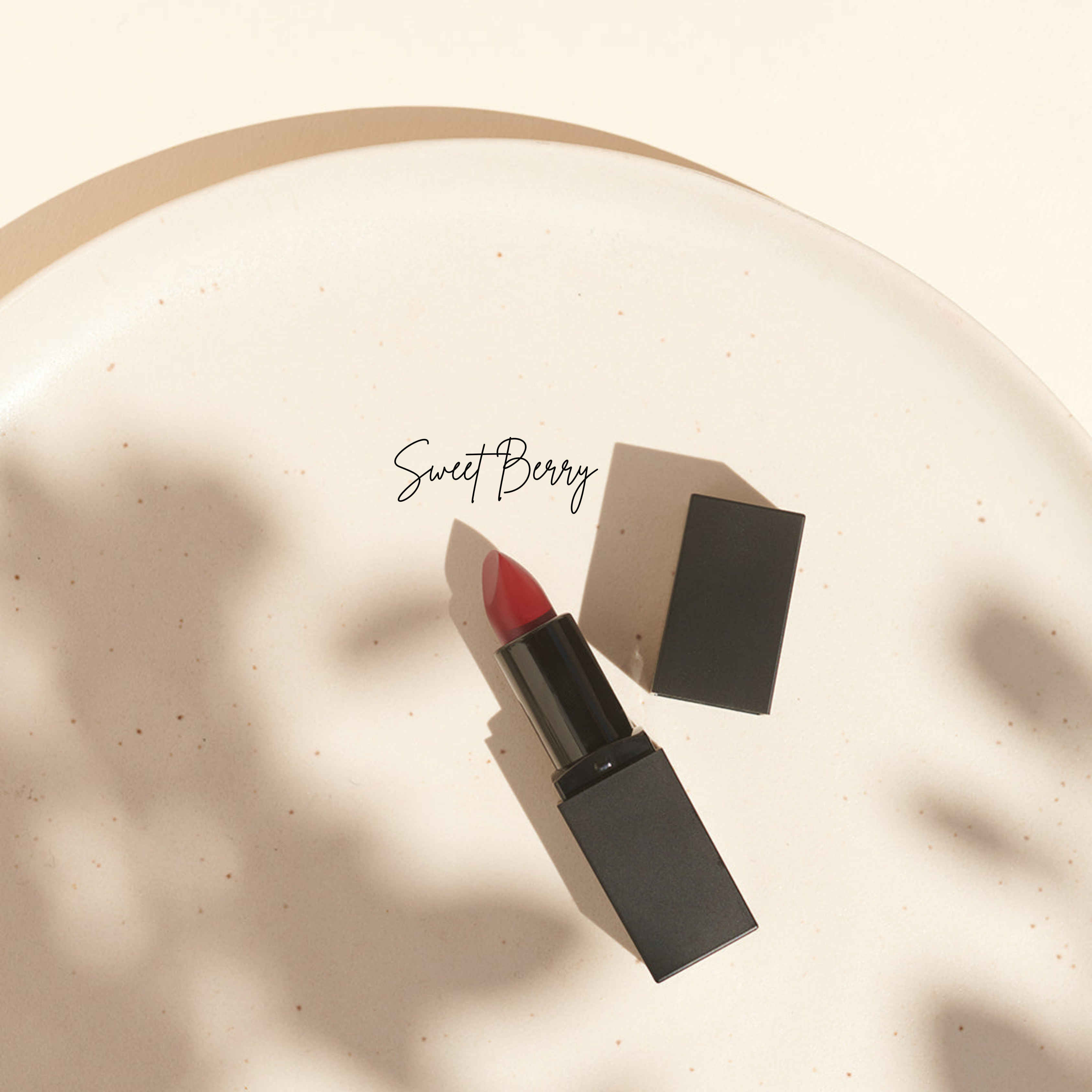 Roter Lippenstift in einer schwarzen Tube auf einem Keramikteller, mit Sweet Berry in Schreibschrift - Thats me Organic® tierversuchsfreie Lippenstifte vereint Stil und Ethik für deine natürliche Lippenpflege.