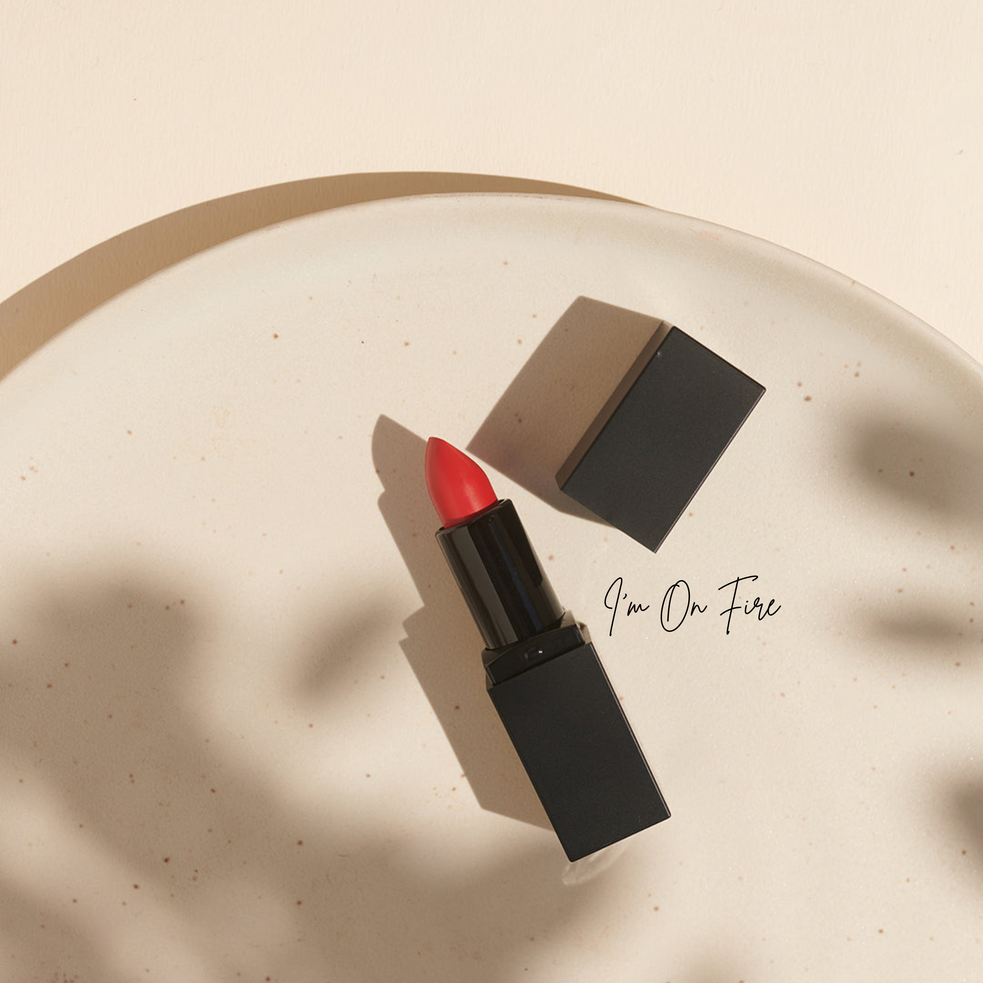 Roter Lippenstift mit schwarzer Hülle und Kappe auf einem runden weißen Teller, daneben der Text "Im On Fire". Aus der veganen Bio-Lippenstifte Kollektion für natürliche Lippenpflege von Thats me Organic®, komplett cruelty-free.