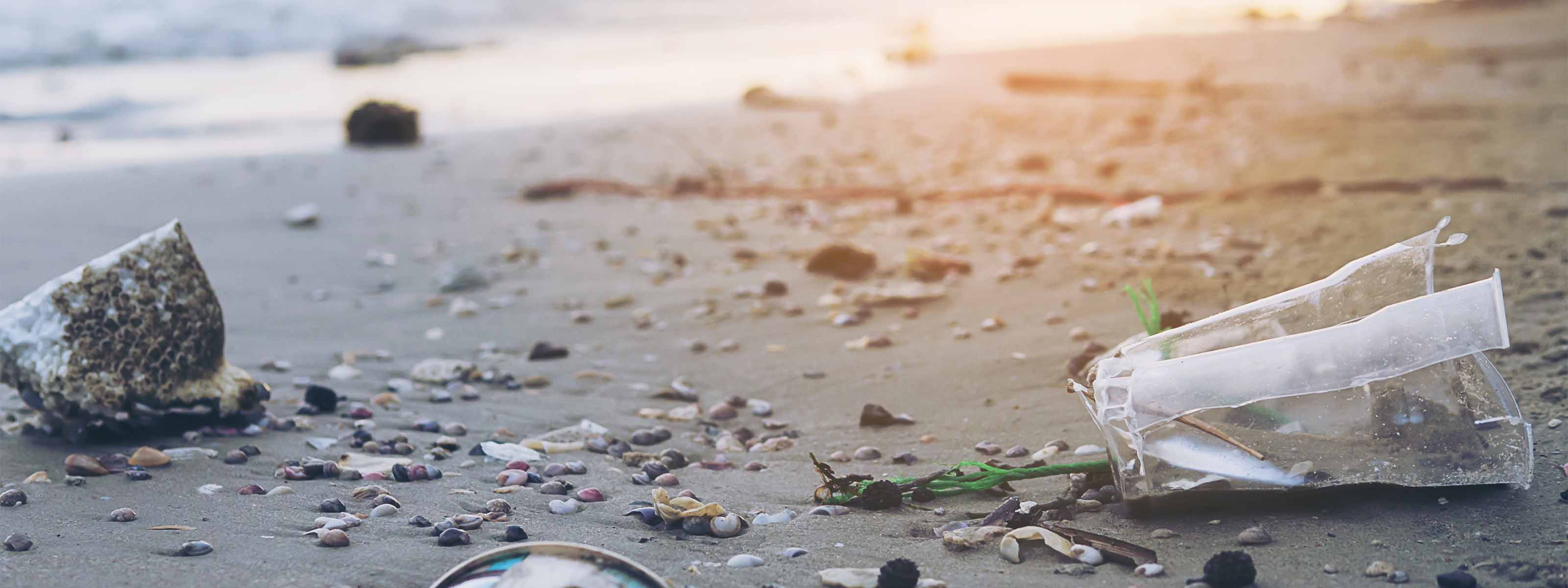 Plastik und anderer Müll verunreinigen einen Sandstrand in der Nähe der Wasserkante bei Sonnenuntergang.