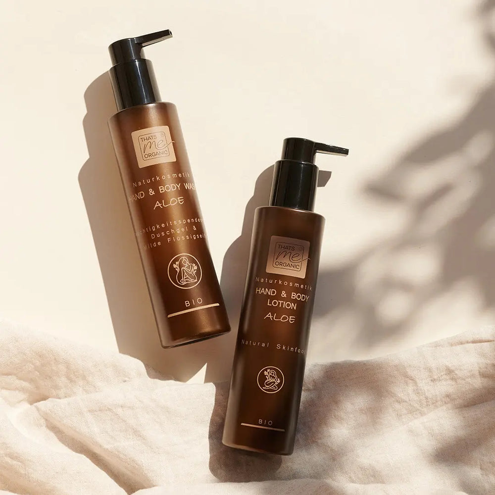 Zwei braune Pumpflaschen von Thats me Organic® Bio Hand & Body Wash und Bio Hand & Bodylotion, beides Naturkosmetik-Produkte, stehen auf einem weichen beigen Stoffhintergrund.