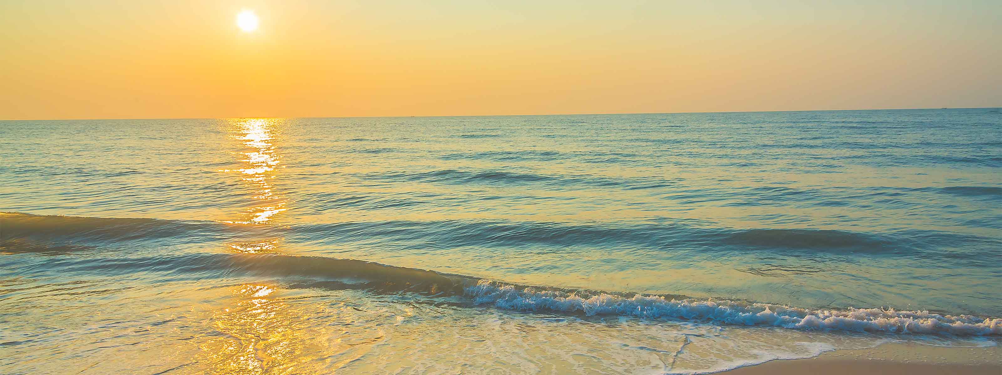 Goldener Sonnenuntergang über einem ruhigen Meer mit sanften Wellen, die auf einen Sandstrand rollen.