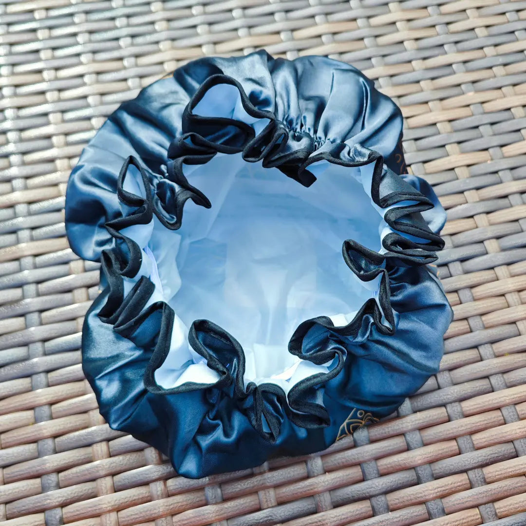 Eine blaue Satinhaube mit weißem Futter von Thats me Organic®, ideal für die Curly-Girl-Methode oder Plopping, liegt offen auf einer geflochtenen Rattanfläche.