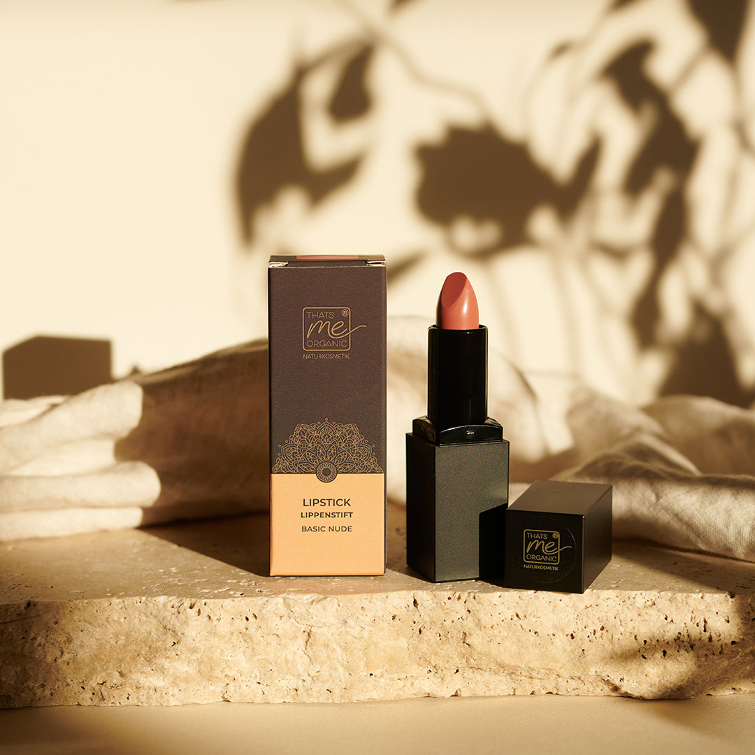 A Thats me Organic® Bio-Lippenstift in Nude und seine Verpackung liegen auf Stein mit sanften Schatten und beigem Stoff im Hintergrund - der Fokus liegt auf natürlicher, veganer Lippenpflege.