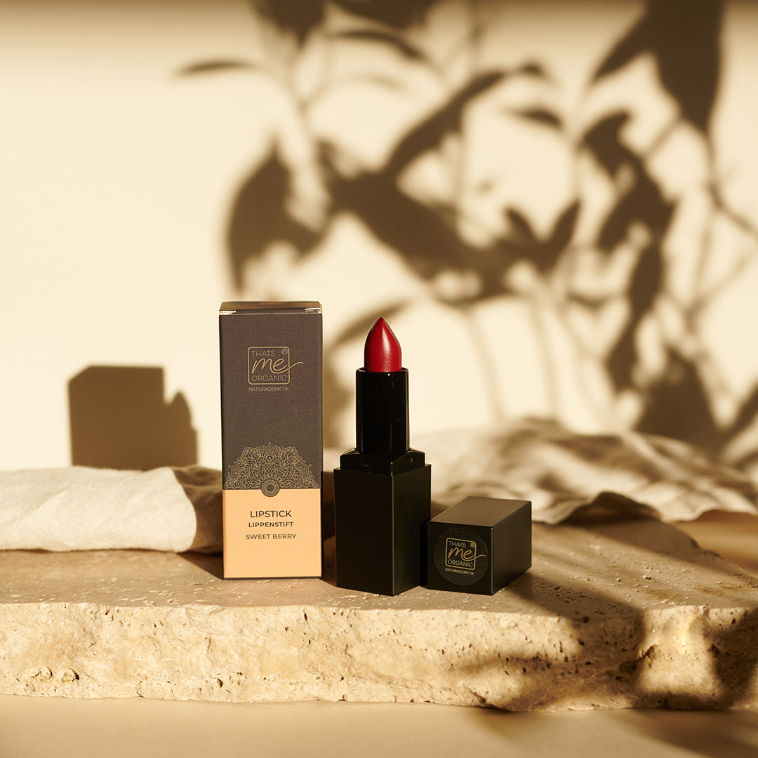 Ein roter Lippenstift in einer schwarzen Tube neben der Schachtel, ausgestellt auf einem Stein mit sanften Schattierungen - ein elegantes Highlight aus der grausam-freien Lippenstiftkollektion von Thats me Organic® für natürliche Lippenpflege.