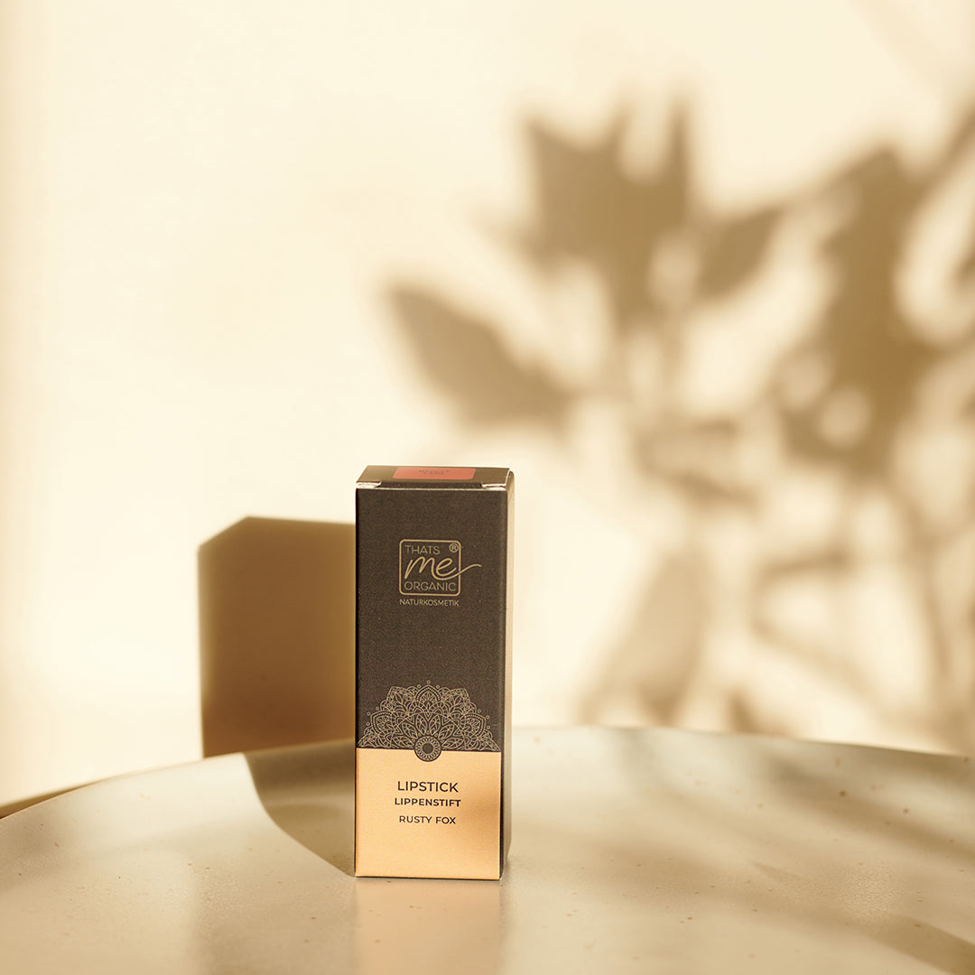 Eine Thats me Organic® Lippenstiftbox sitzt auf einer hellen Fläche mit sanften Schatten und Sonnenlicht und hebt die veganen Bio-Lippenstifte der Marke für natürliche Lippenpflege hervor.