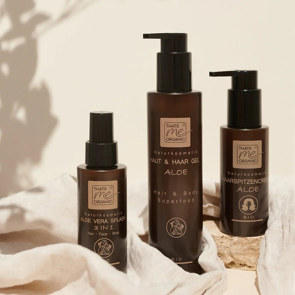 Drei braune Flaschen Thats me Organic® aloe skinincare auf einem leichten Stoffhintergrund, ideal zur Beruhigung von Haut, die durch trockene Luft oder durch statische Aufladung der Haare strapaziert wird.