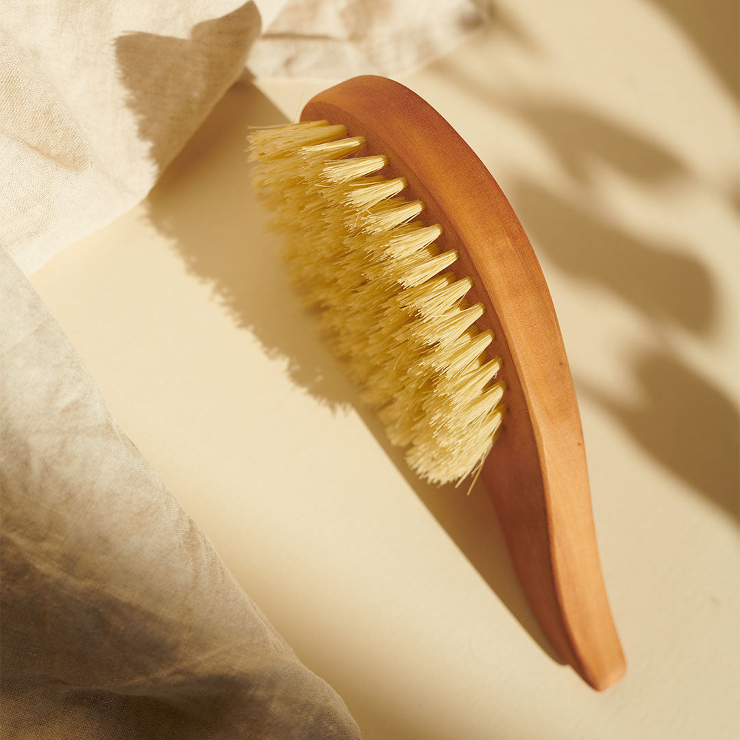 Eine Thats me Organic® Tropfenform Bürste mit hellen Borsten liegt auf beiger Oberfläche im sanften Sonnenlicht - perfekt zur Förderung des Haarwachstums.