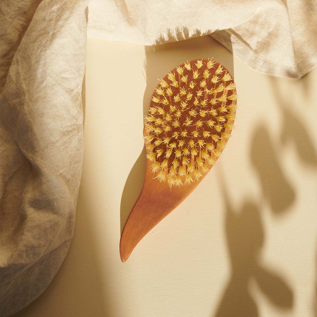 Die Thats me Organic® Holz-Haarbürste in Tropfenform mit dichten Borsten auf cremefarbener Fläche, neben hellem Tuch - die vegane Bürste kann Haarwachstum fördern.