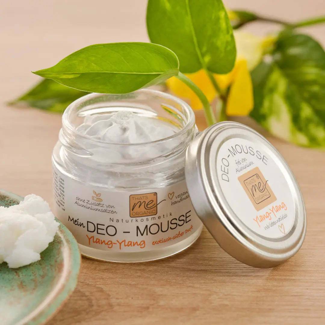 Geöffnete Dose des natürlichen Deodorants Thats me Organic® Bio-Deo-Mousse mit Ylang-Ylang-Duft, neben einer grünen Blattpflanze platziert.