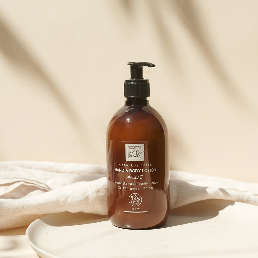 Braune Pumpflasche der Thats me organic® Bio Hand & Body Lotion mit Aloe auf einem weißen Tuch, vor einem beigen Hintergrund. Ideal für Naturkosmetik-Liebhaber.
