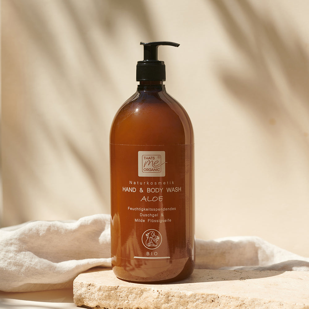 Bernsteinfarbene Flasche Thats me organic® Bio-Hand & Body Wash Naturkosmetik mit schwarzer Pumpe, auf ein leichtes Tuch gestellt.