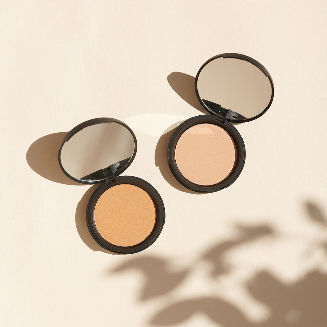 Zwei offene Thats me Organic® Bio-Powder Kompaktpuder mit Spiegeln liegen auf einer hellbeigen Oberfläche und werfen weiche Schatten. Genießen Sie einen mattierenden Effekt mit diesem veganen Beauty-Essential.