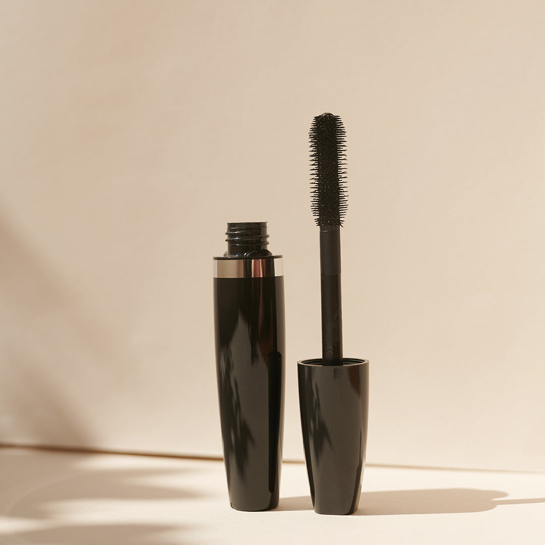 Die Thats me Organic® Black Mega Volume Mascara Tube mit offenem Stift steht aufrecht auf einer beigen Oberfläche in sanftem Licht. Hergestellt mit natürlichen Inhaltsstoffen für schwungvolle Wimpern und einen natürlichen Look.