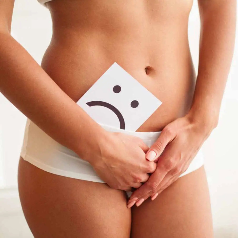Eine Frau in Unterwäsche hält ein Schild mit einem traurigen Gesicht über ihren Unterleib und betont damit die Notwendigkeit von sanfter Intimpflege und natürlichen Intimreinigern von Thats me Organic® für Wohlbefinden und Schutz.