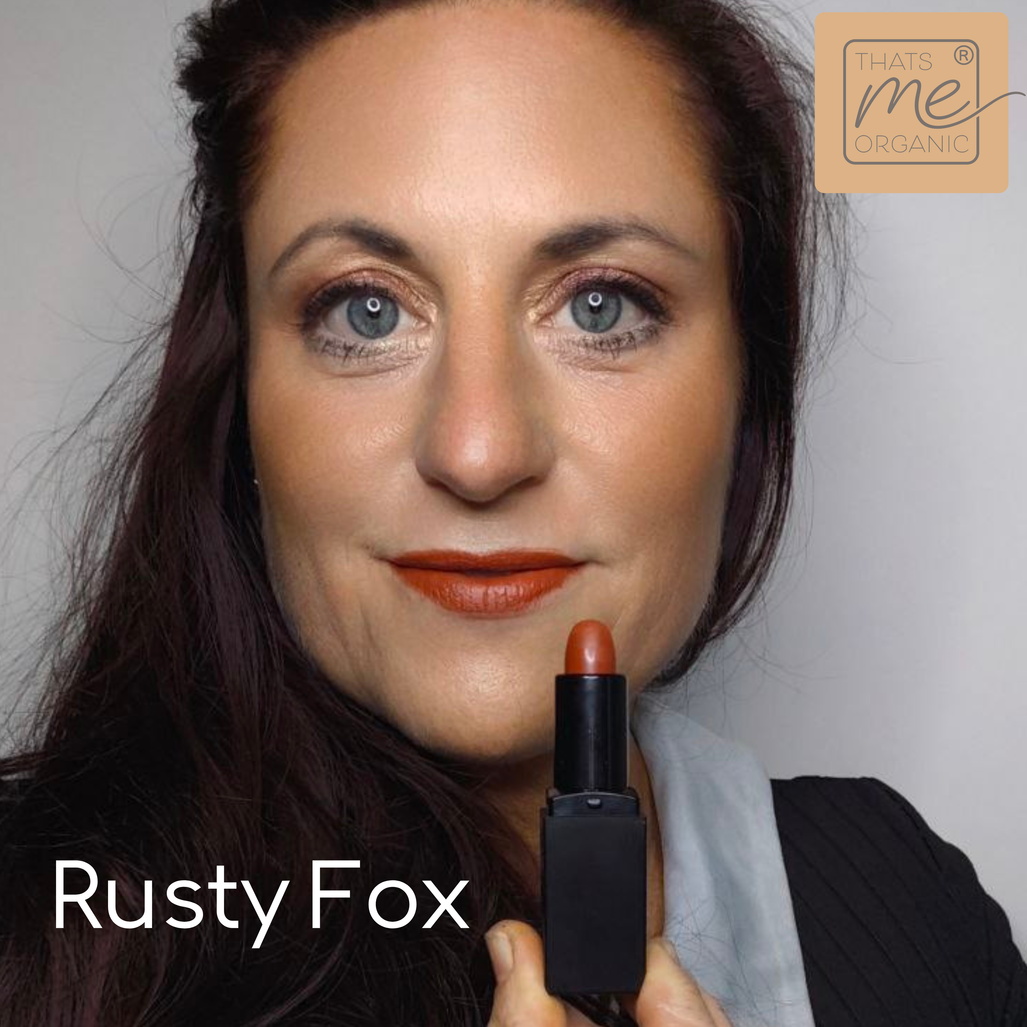 Frau mit blauen Augen trägt Thats me Organic® Rusty Fox orange-braunen Lippenstift, hält die veganen Bio-Lippenstifte zur natürlichen Lippenpflege an ihr Gesicht.