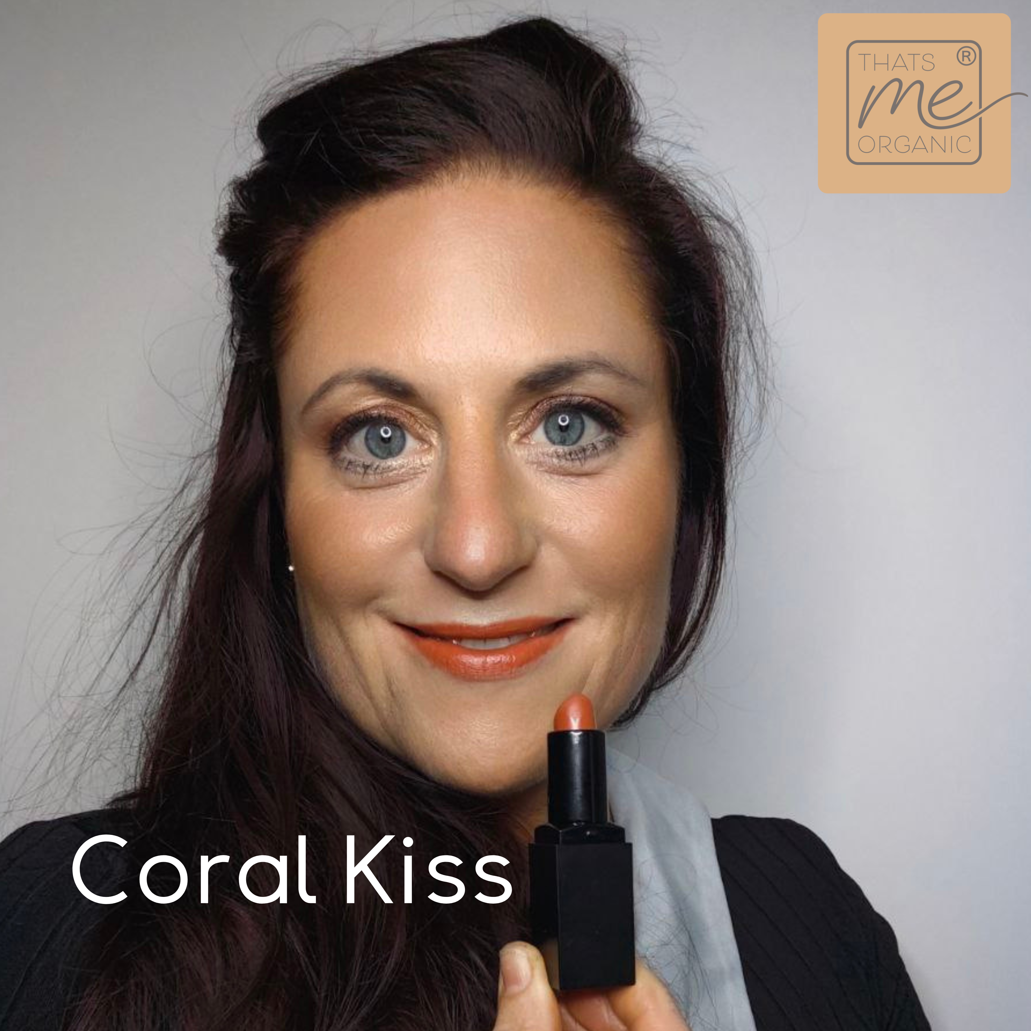 Eine Frau mit langen braunen Haaren lächelt und hält einen korallenroten Lippenstift. Text: Coral Kiss und Thats me Organic®-entdecke unsere tierversuchsfreien Lippenstifte und natürliche Lippenpflege.