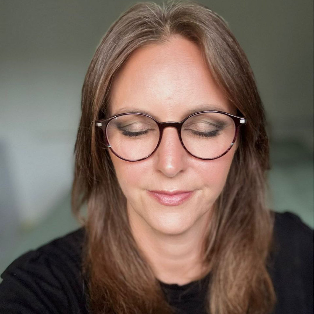 Frau mit braunen Haaren und Brille, Augen geschlossen, trägt ein schwarzes Oberteil bei gedämpfter Innenbeleuchtung und präsentiert Thats me Organic® vegane und titandioxidfreie Naturkosmetik Lidschatten.