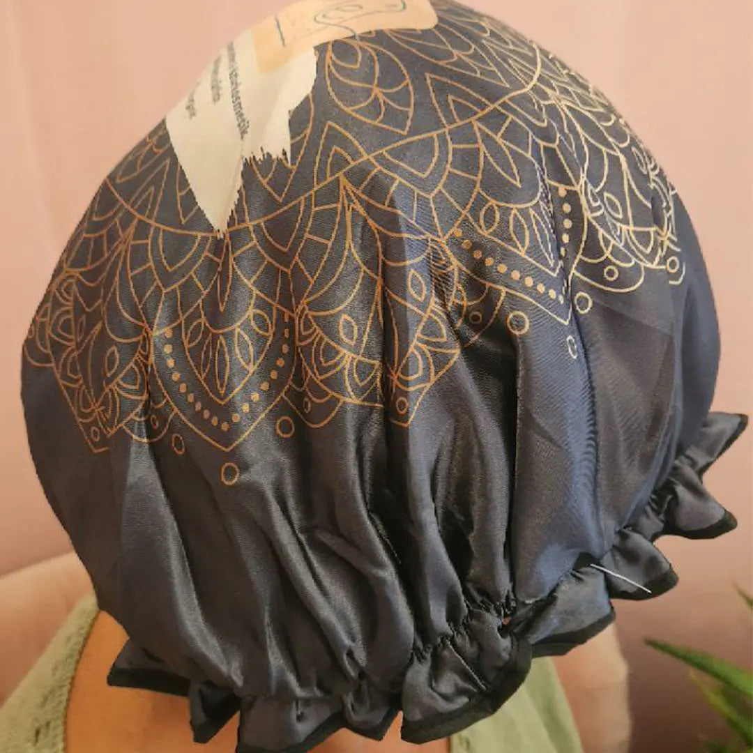 Jemand trägt eine Thats me Organic® Haube aus dunklem Satin mit goldenen Mandalamustern und gerüschten Rändern, ideal für die Curly-Girl Methode oder als stylische Pflanzenhaarfarbe Haube, von hinten gesehen.