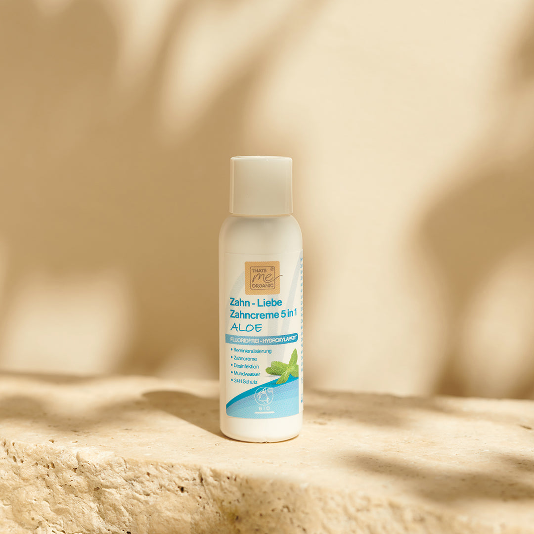 Eine Flasche Thats me organic® 5-in-1 Aloe Vera BIO-Zahncreme steht auf einer sonnenbeschienenen Steinfläche mit beigem Hintergrund.