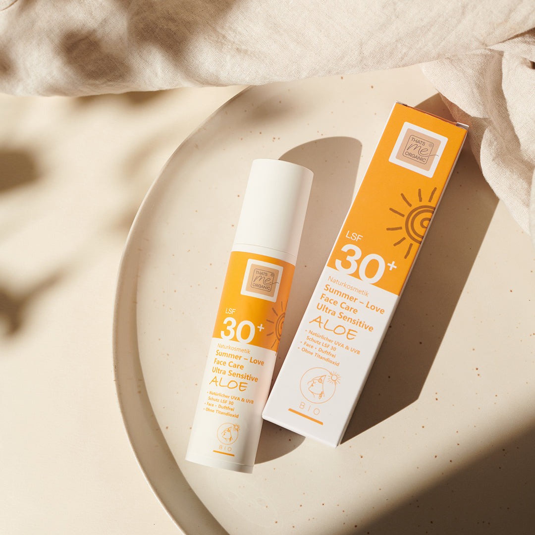 Eine Flasche und eine Schachtel Thats me Organic® Bio Sonnencreme LSF 30+ ohne Titandioxid mit Aloe, angeordnet auf einem beigen Teller im Sonnenlicht.