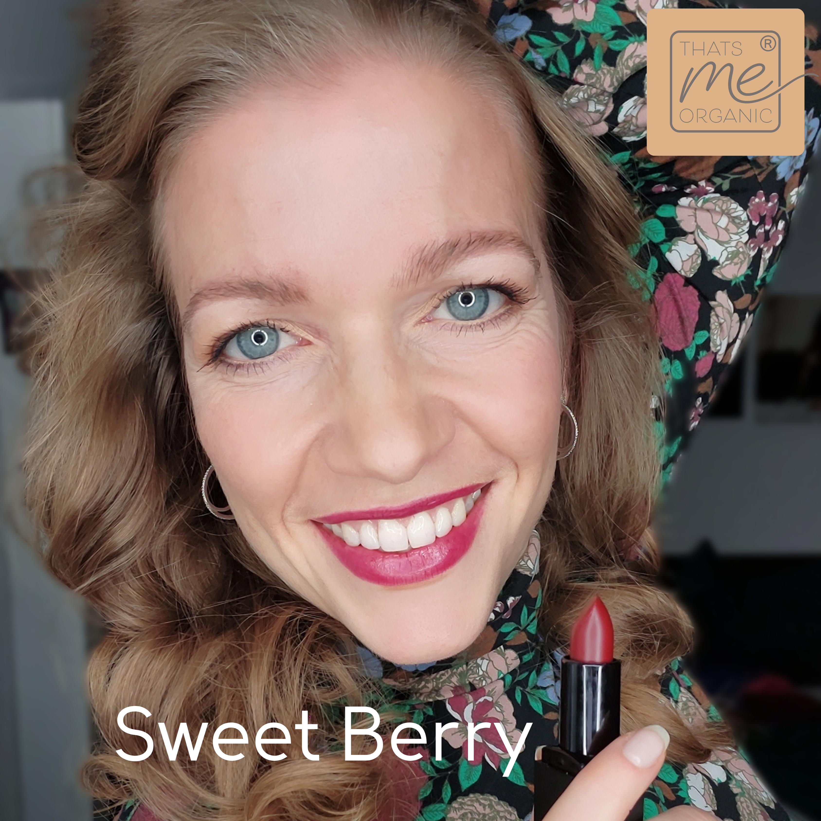 Eine lächelnde Frau mit gewelltem Haar hält einen roten Lippenstift in der Hand; der Text lautet Sweet Berry und Thats me Organic® und hebt vegane Bio-Lippenstifte hervor.