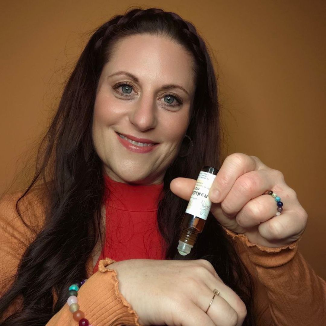 Eine lächelnde Frau trägt vor einem orangefarbenen Hintergrund das Thats me Organic® NATRUE-zertifizierte Serum aus einer kleinen Flasche auf ihren Handrücken auf.