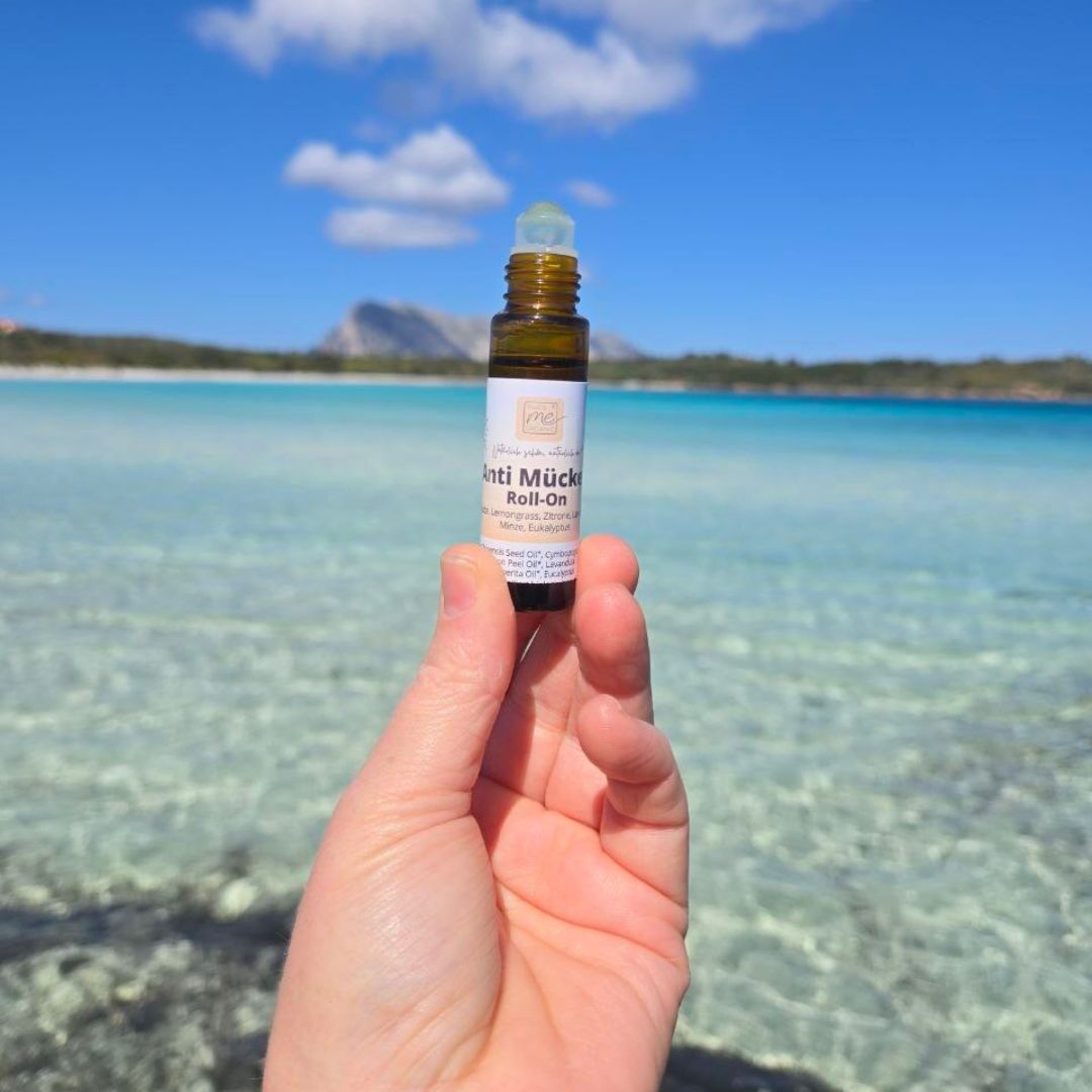 Hand hält ein Thats me Organic® Anti-Mücken-Roll-On über klarem blauen Wasser mit Bergen im Hintergrund - der natürliche Mückenschutz und das ideale Hausmittel gegen Mücken für unterwegs.