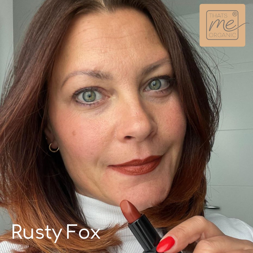 Eine Frau mit schulterlangen braunen Haaren trägt rostbraunen Lippenstift auf; Text: Rusty Fox by Thats me Organic®-featuring tierversuchsfreie Lippenstifte für natürliche Lippenpflege.