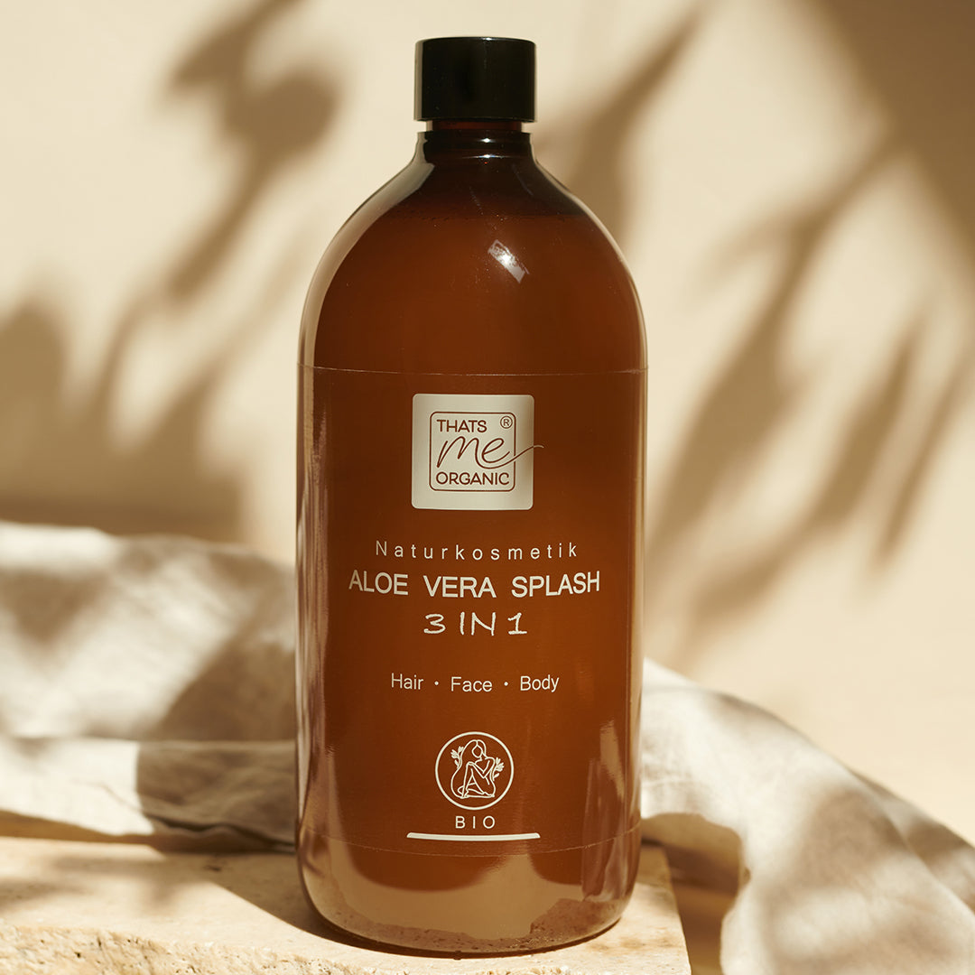 Eine große braune 1000ml Nachfüllflasche von Thats me organic® Bio Aloe Vera Splash 3 in 1 Naturkosmetik für Haare, Gesicht und Körper ist auf einem beigen Hintergrund abgebildet.