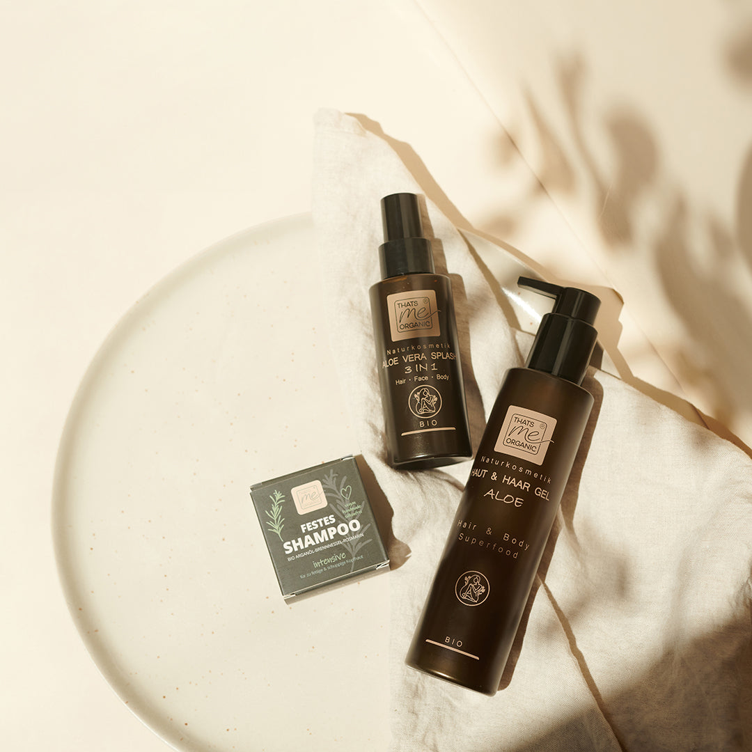 Thats me Organic® Aloe Vera Shampoo und Kopfhautpflege werden auf einem beigen Tuch in sanftem Sonnenlicht und sanften Schatten präsentiert und bilden eine beruhigende Kulisse für all Ihre Bedürfnisse bei der Anti-Schuppen-Haarpflege und Hautpflege.