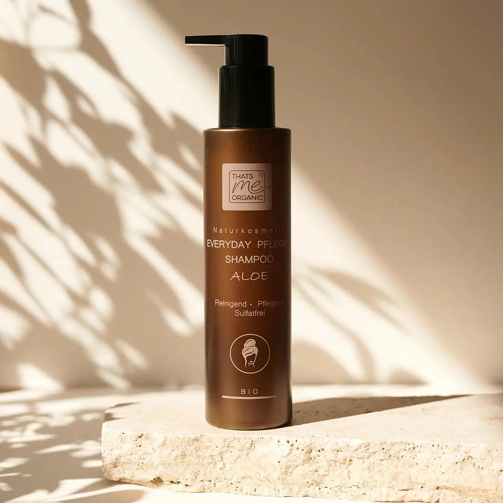 Braune Flasche mit Bio-Aloe-Shampoo mit einer Pumpe, die auf einer Steinfläche im Sonnenlicht steht.