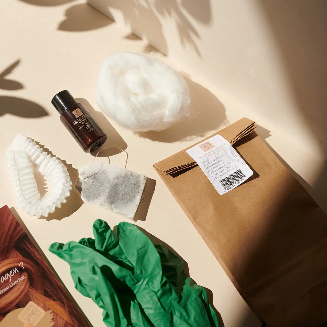 Eine braune Papiertüte, grüne Handschuhe, Watte, Flasche, Teebeutel und Zahnpflegeartikel auf einer hellen Oberfläche erinnern an die Essenz von Thats me Organic® natürliche Haarpflege mit einem Hauch von Pflanzenhaarfarbe und Bio-Shampoo für eine gesunde tägliche Routine.