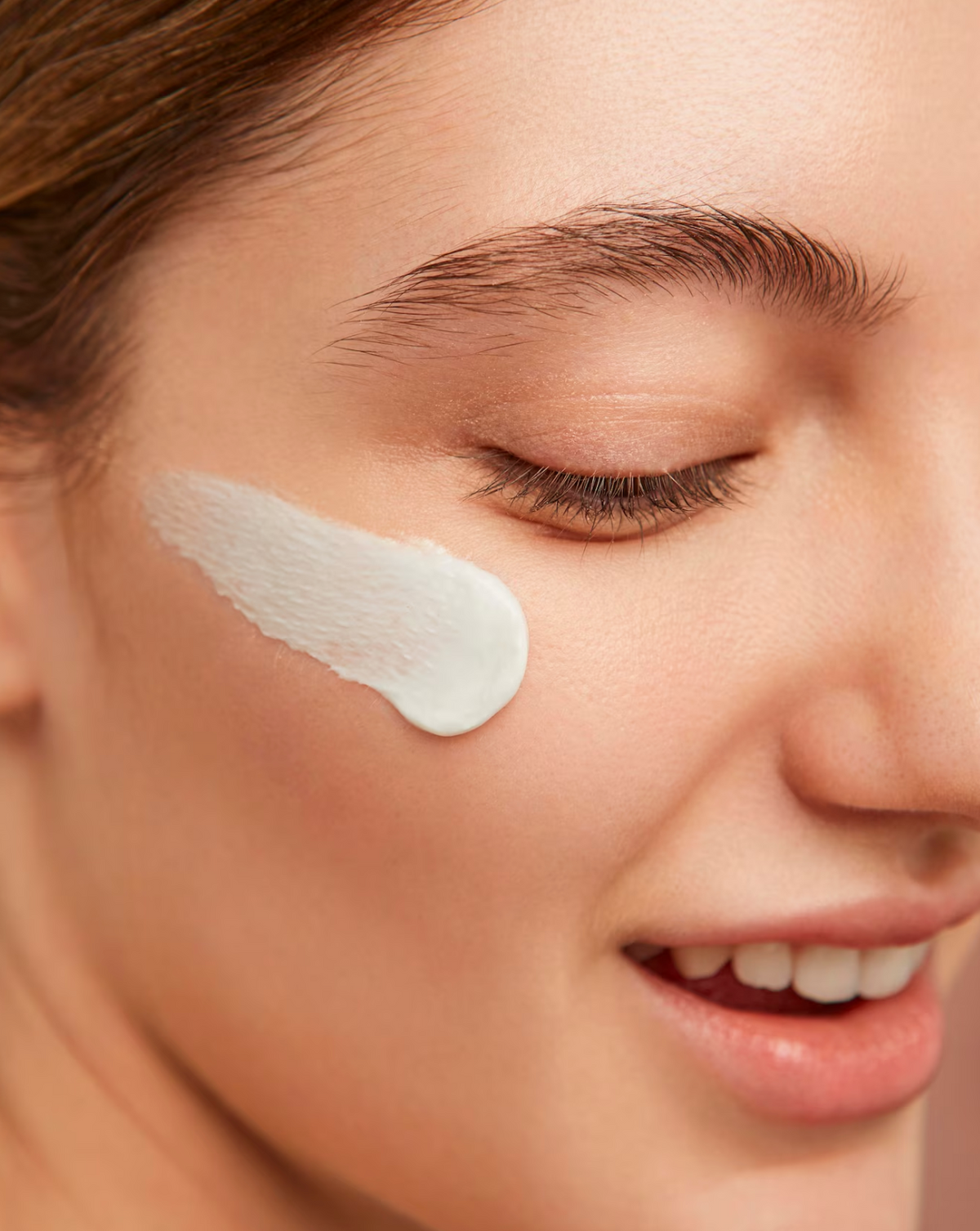 Eine lächelnde Frau mit einem Klecks weißer Creme auf der Wange, Nahaufnahme ihres Gesichts.