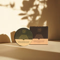 Thats me Organic® Compact Bronzing Powder mit natürlichen Inhaltsstoffen, abgebildet in seiner Box auf einer beigen Oberfläche mit dekorativen Schatten im Hintergrund.