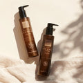 Zwei braune Pumpflaschen von Thats me Organic® Bio Hand & Body Wash und Bio Hand & Bodylotion, beides Naturkosmetik-Produkte, stehen auf einem weichen beigen Stoffhintergrund.