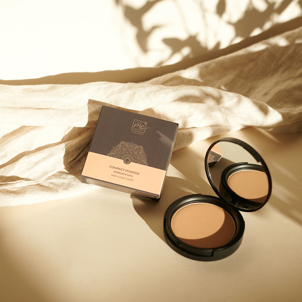 Thats me Organic® mattierendes Bio-Puder in einem eleganten, schwarz verspiegelten Etui, das neben der Schachtel auf beigem Stoff mit weichen Schatten abgebildet ist.
