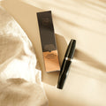 Eine schwarze Thats me Organic® Mega Volume Mascara-Tube und die dazugehörige Schachtel werden auf einem cremefarbenen Stoff in sanftem Sonnenlicht zur Schau gestellt und unterstreichen die Eleganz dieser Bio-Wimperntusche.