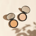 Zwei offene Thats me Organic® Bio-Powder Kompaktpuder mit Spiegeln liegen auf einer hellbeigen Oberfläche und werfen weiche Schatten. Genießen Sie einen mattierenden Effekt mit diesem veganen Beauty-Essential.
