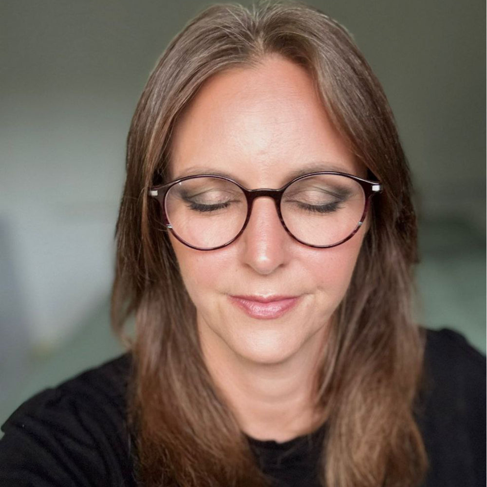 Frau mit braunen Haaren und Brille, Augen geschlossen, trägt ein schwarzes Oberteil bei gedämpfter Innenbeleuchtung und präsentiert Thats me Organic® vegane und titandioxidfreie Naturkosmetik Lidschatten.