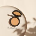 Ein offenes, beigefarbenes Thats me Organic® Puderdöschen sitzt auf einer hellen Platte mit "Non Glossy Beige" daneben in weichem Licht - ideal für einen mattierenden Effekt mit diesem veganen Bio-Puder.