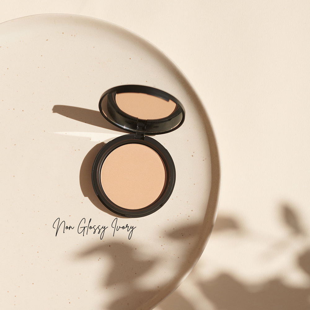 Ein offener Kompaktpuder von Thats me Organic® vegan Bio-Powder in nicht-glänzendem Elfenbein liegt auf einer hellen Oberfläche, wirft weiche Schatten und sorgt für einen mattierenden Effekt.
