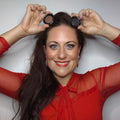 Frau in rotem Oberteil lächelt und hält zwei runde Thats me Organic® Naturkosmetik Lidschatten-Dosen über ihrem Kopf vor weißem Hintergrund.