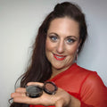 Eine Frau mit rotem Oberteil lächelt, während sie zwei geöffnete Thats me Organic® Naturkosmetik Lidschatten-Dosen in der Hand hält, von denen eine den auffälligen Farbton Metallic Copper aufweist.