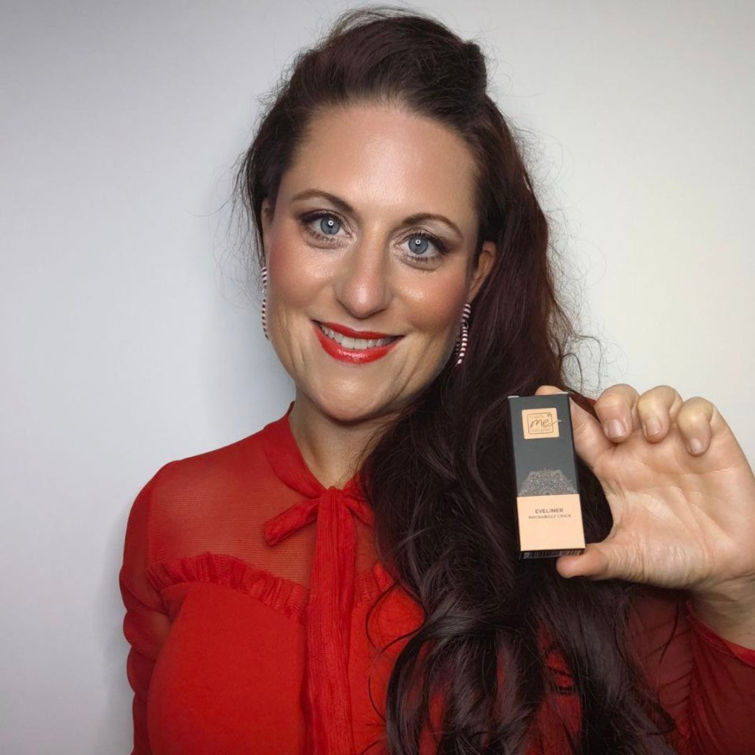 Eine Frau in einem roten Top lächelt, während sie eine Thats me Organic® Bio Eyeliner-Dose - ideal für empfindliche Augen - vor einem schlichten Hintergrund hochhält.